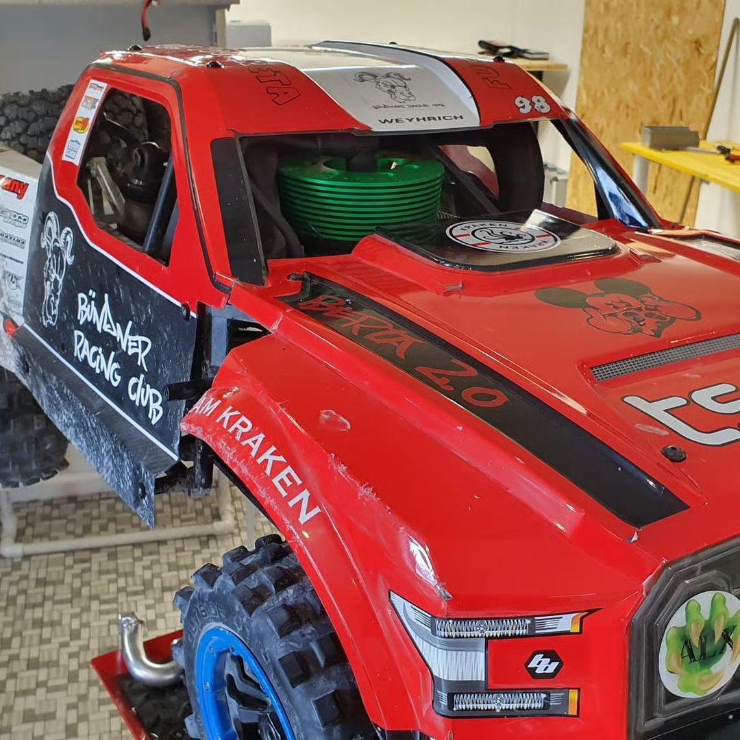 Red off-road model truck with various decals and logos in a workshop setting.