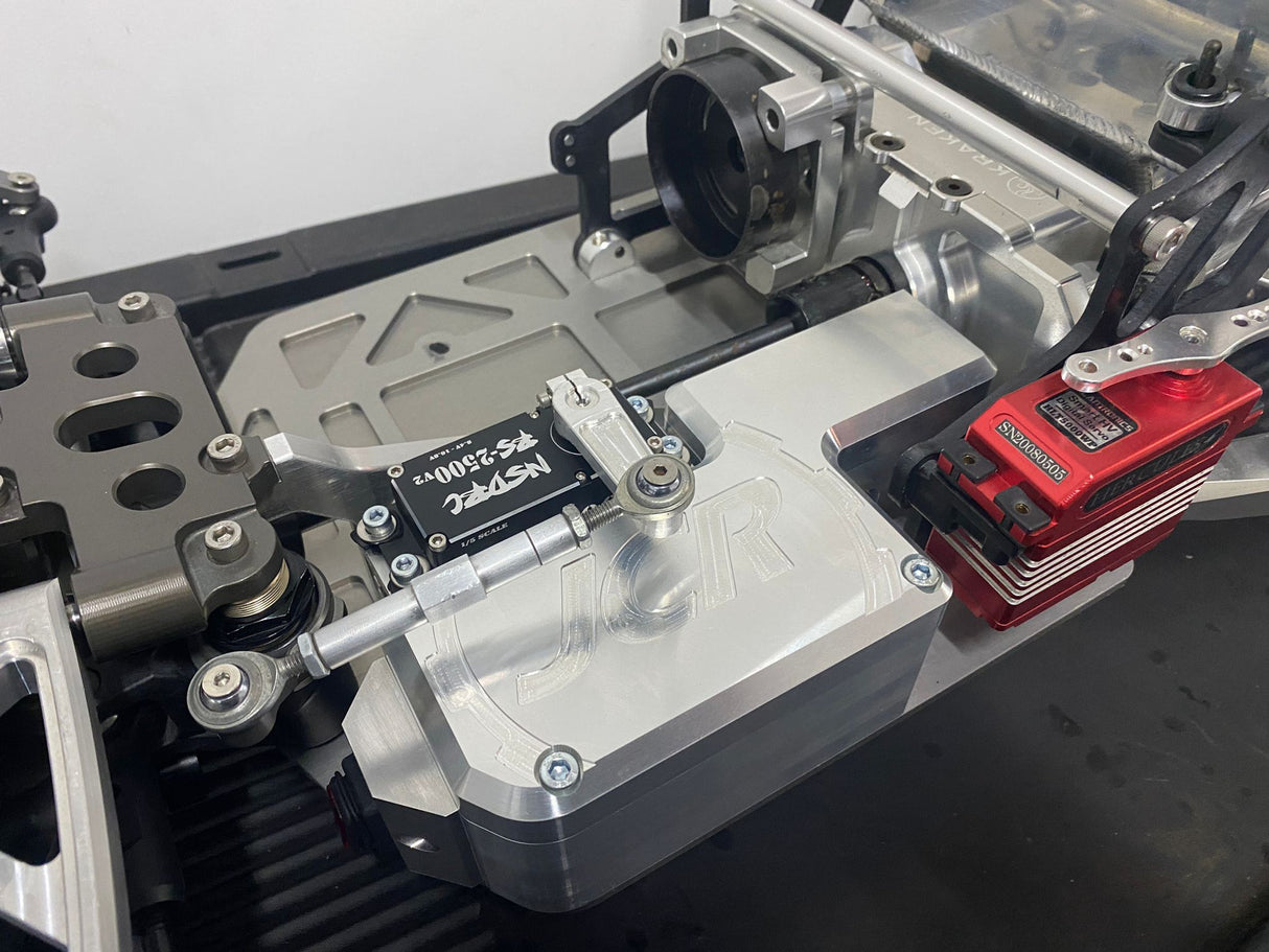 A silver CNC-machined aluminum battery box with a slide-on lid, mounted on a remote control vehicle chassis with servo stands and a red battery pack.