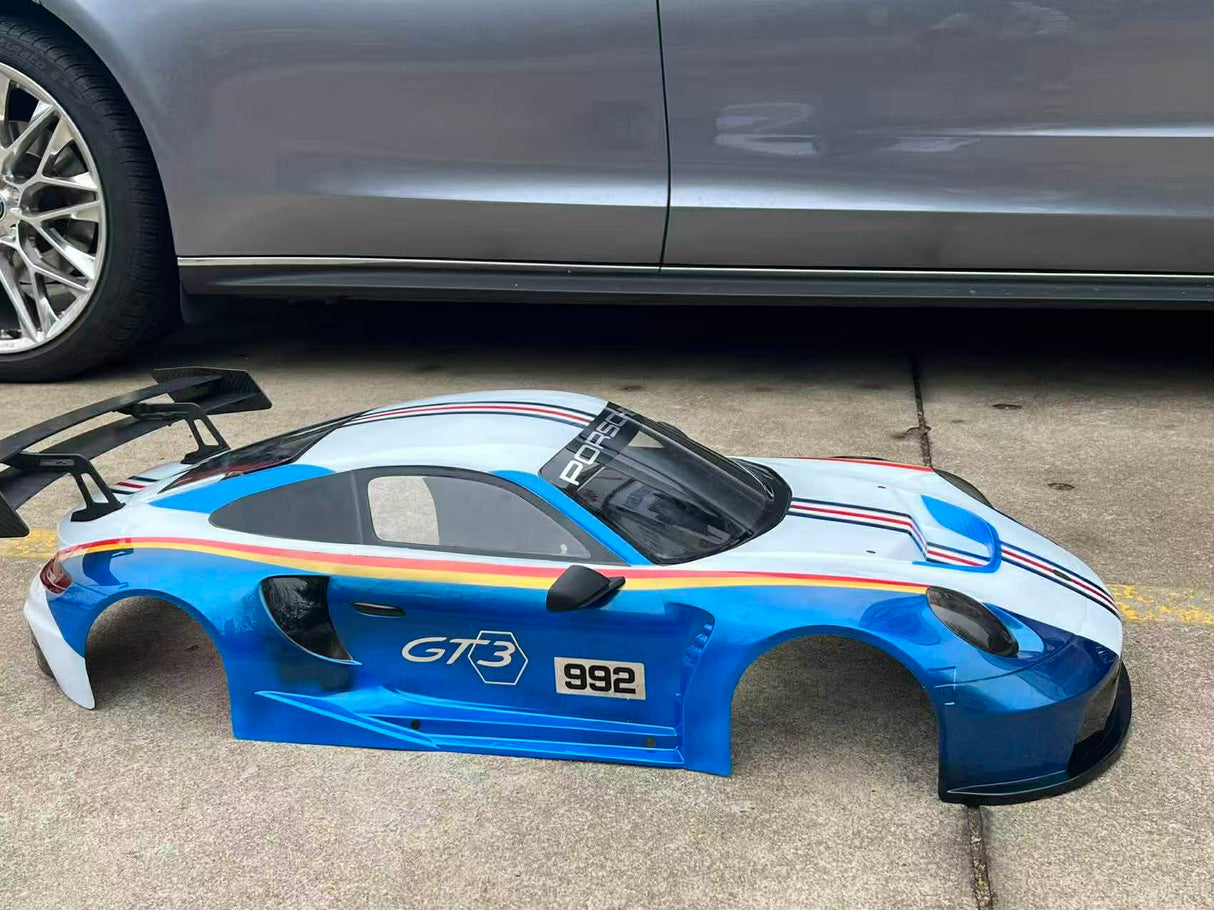 Blue car body shell with 'GT3' and '992' branding on a concrete surface.