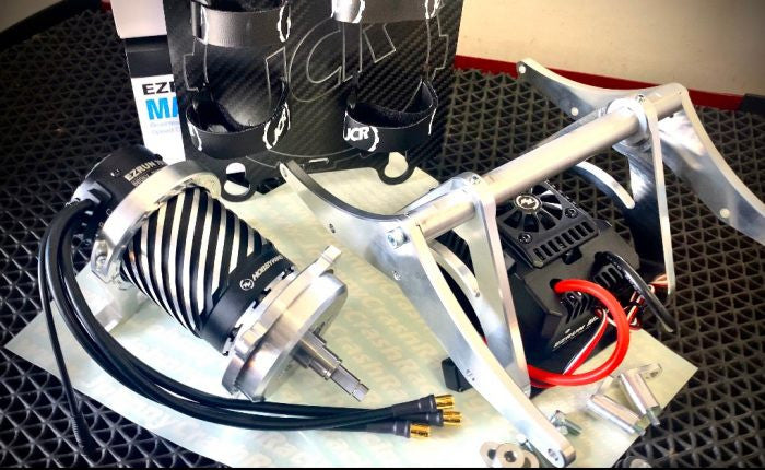 Remote control truck conversion kit components laid out on a table, including aluminum and carbon fiber parts, wiring, and unattached motor and ESC.