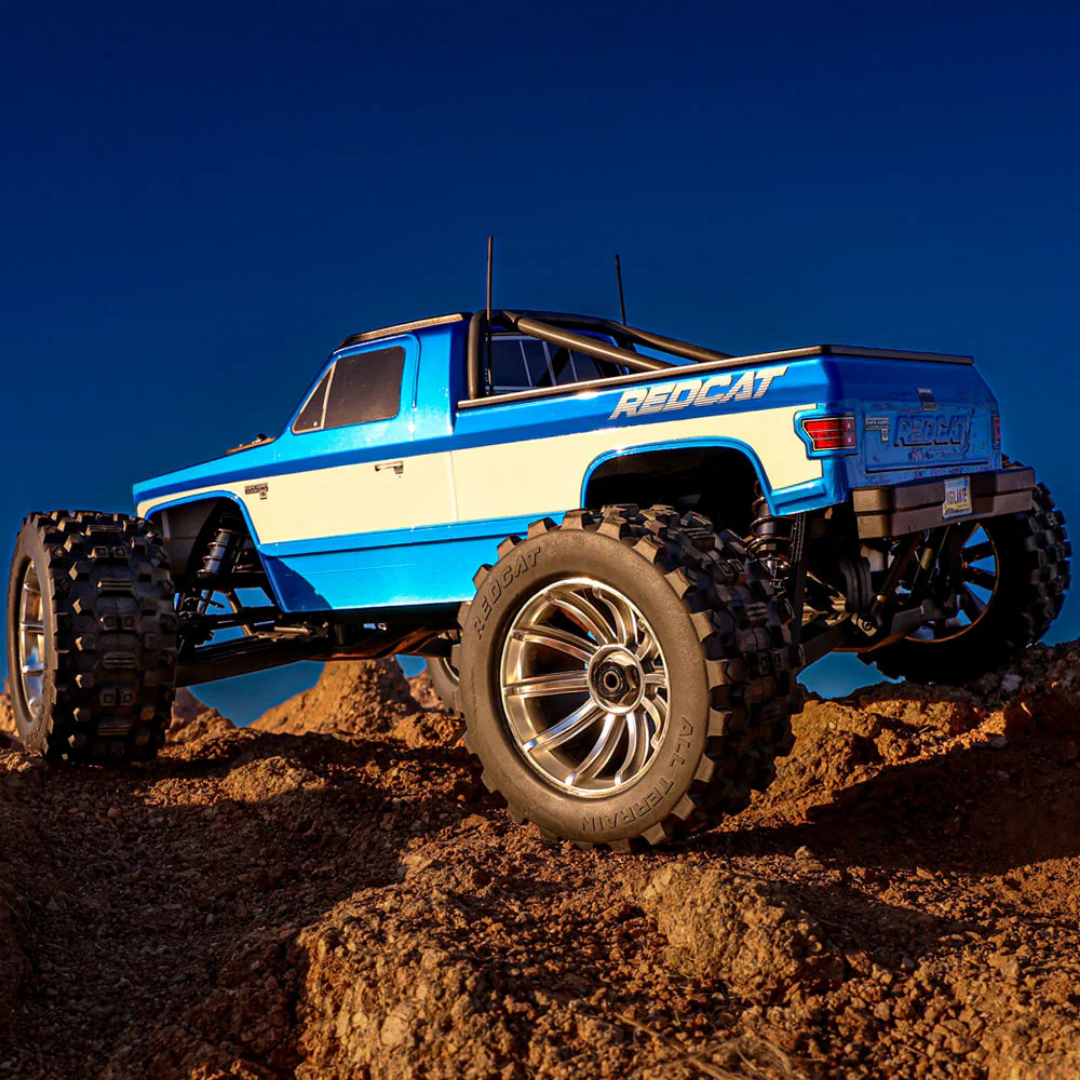 Blue and white off-road truck on a dirt surface with a clear blue sky.