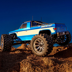 Blue and white off-road truck on a dirt surface with a clear blue sky.