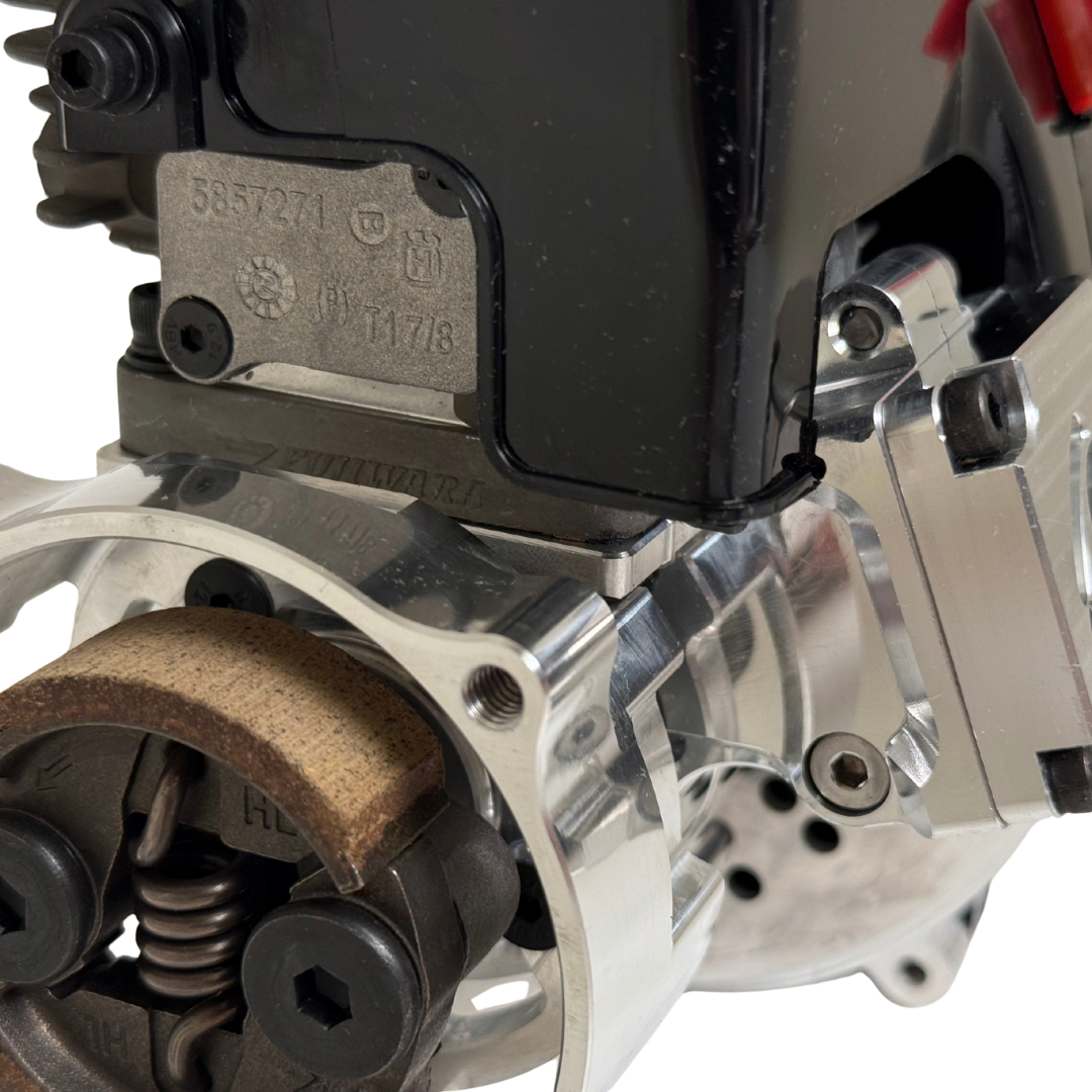 Close-up of the HPRC 38cc race ported Fujiwara engine's manufacturer label plate above the raw silver billet reed case and clutch shoe