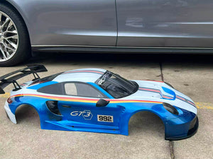 Blue car body shell with 'GT3' and '992' branding on a concrete surface.