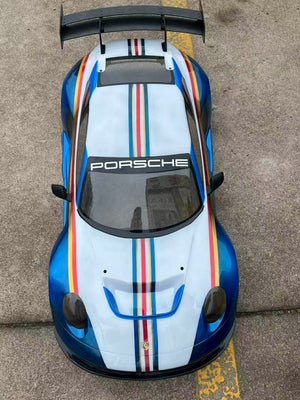 Top view of a Porsche car with a white hood featuring red, blue, and yellow stripes on a concrete surface.