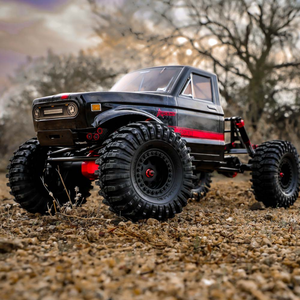 Black and red off-road RC truck on a dirt surface with a blurred natural background