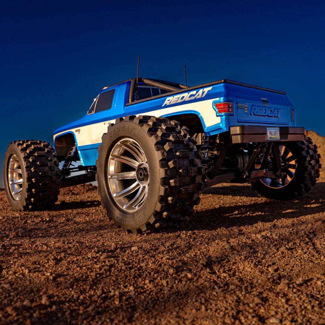 Blue and white RC truck with large wheels on a dirt surface under a clear blue sky.