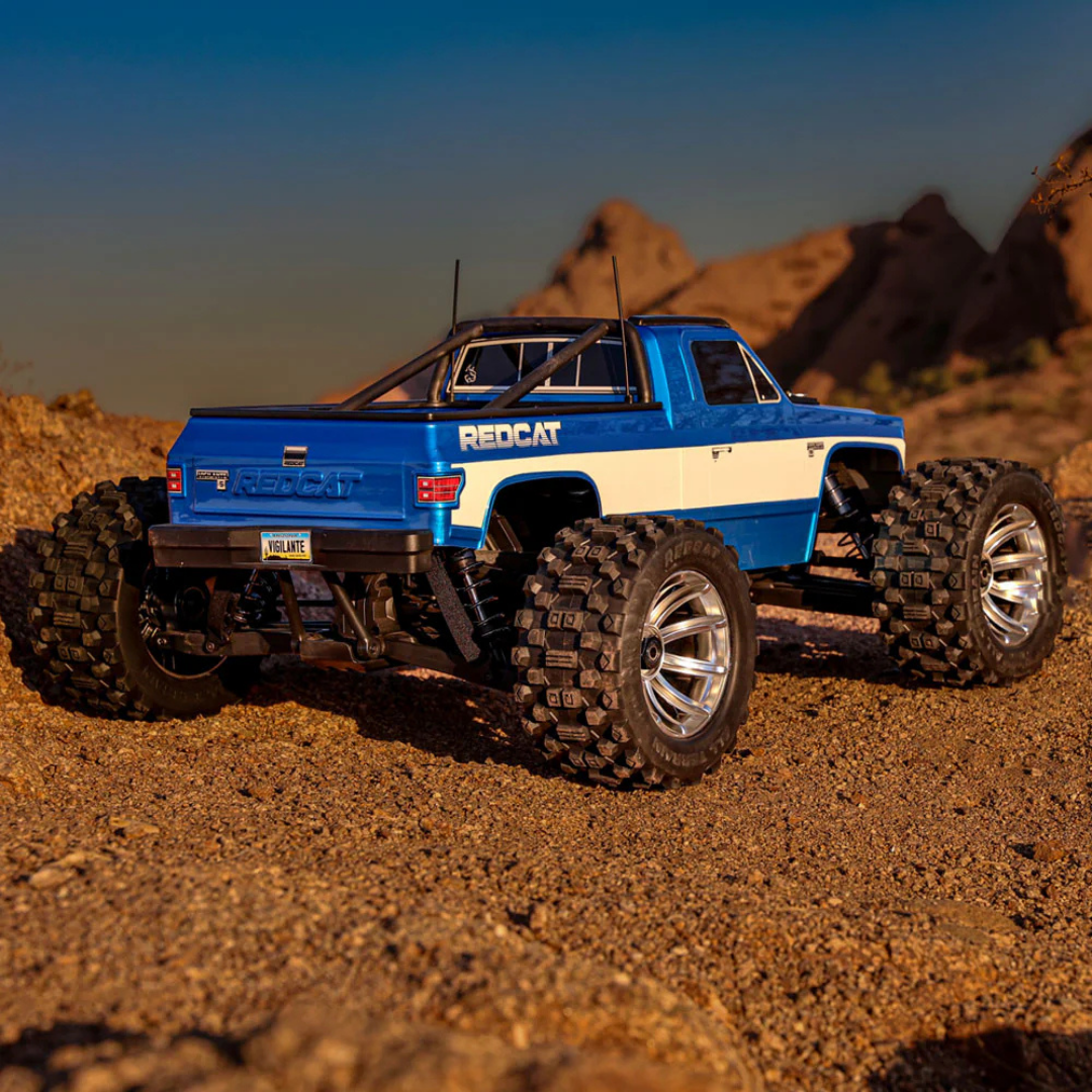 Blue and white RC truck on a desert landscape with rocky formations.